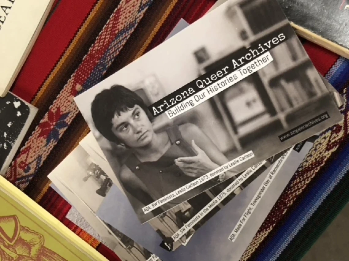 a photograph of a person with a label that says "arizona queer archives: building our histories together" on it sitting on top of an archive of items