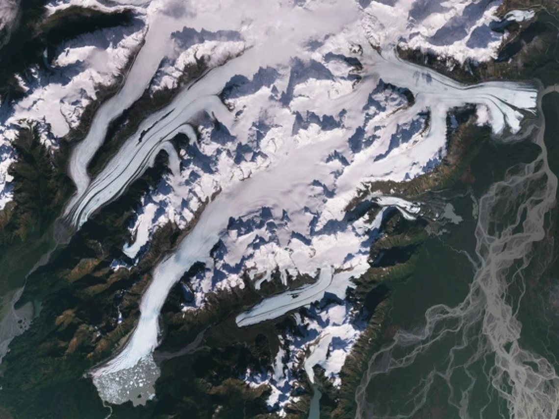 A satellite image of glaciers in Alaska shows white flows of ice surrounded by dark green mountain ridges